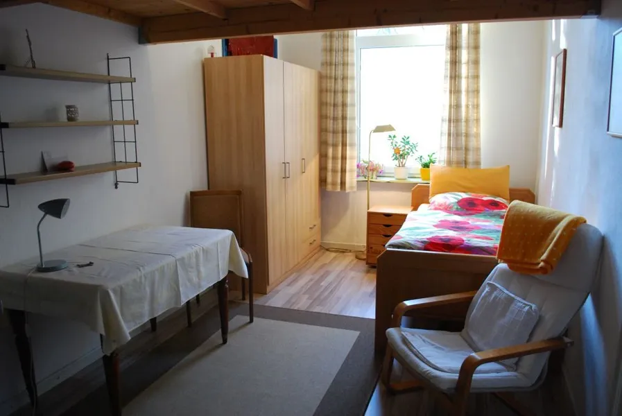 Einzelzimmer der Pension Halstrup mit Bett, Sessel und Tisch am Fenster